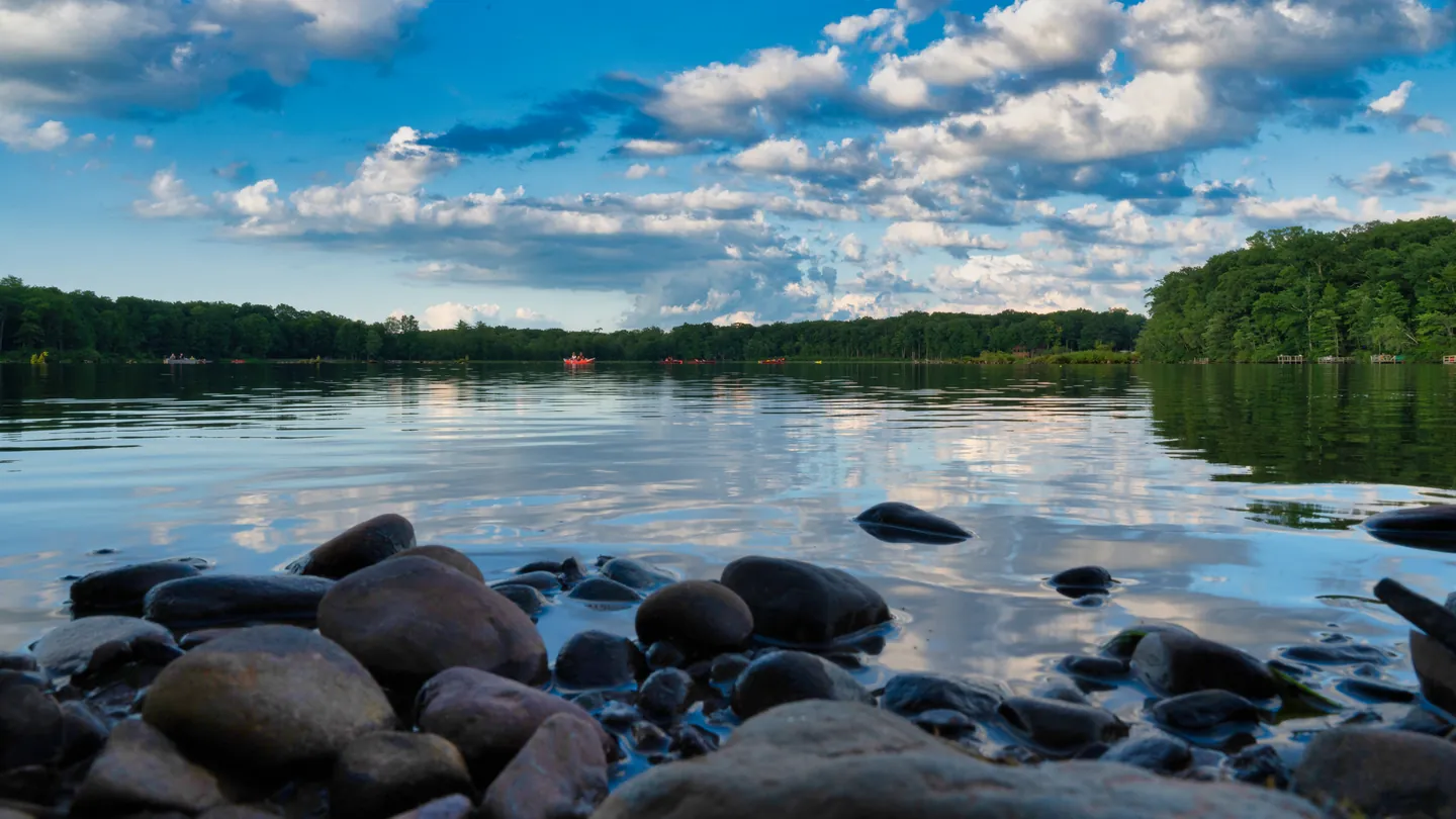 The lake from its rocky shore under summer clouds